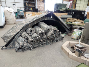 Inside room with Combat Tent full of tents ready to be popped up. Color is small squares of two different grays and white mixed throughout the whole tent. One hole opening .